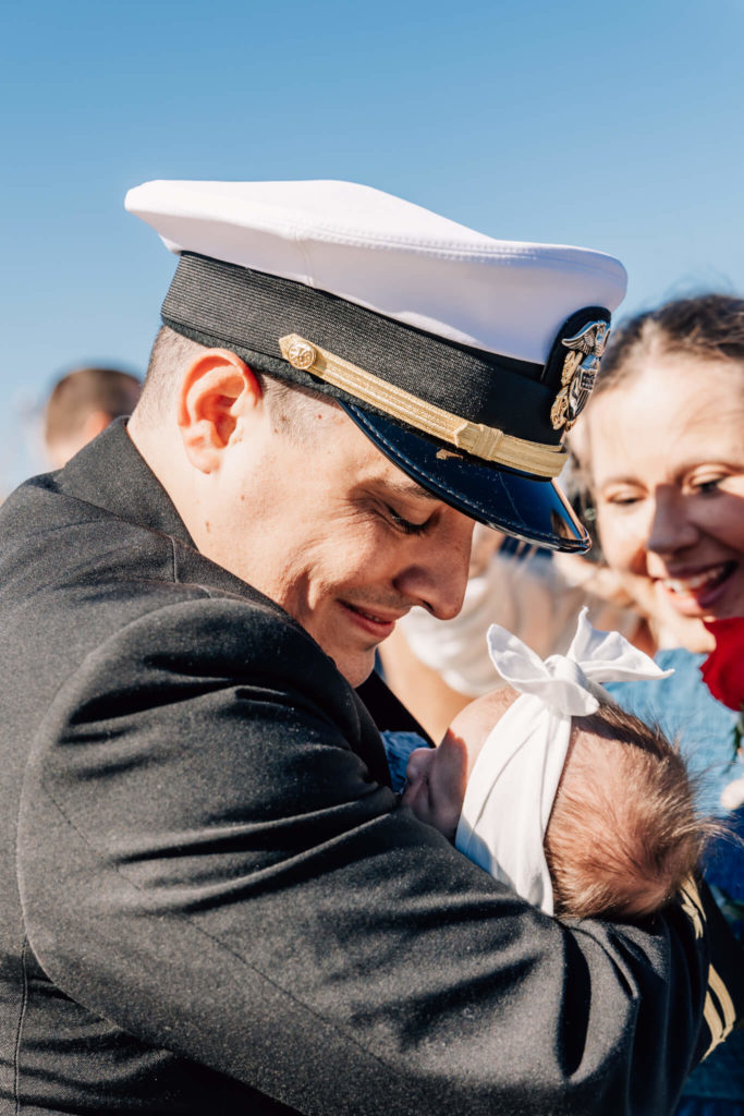 Naval officer looks down at baby at USS North Dakota military homecoming.